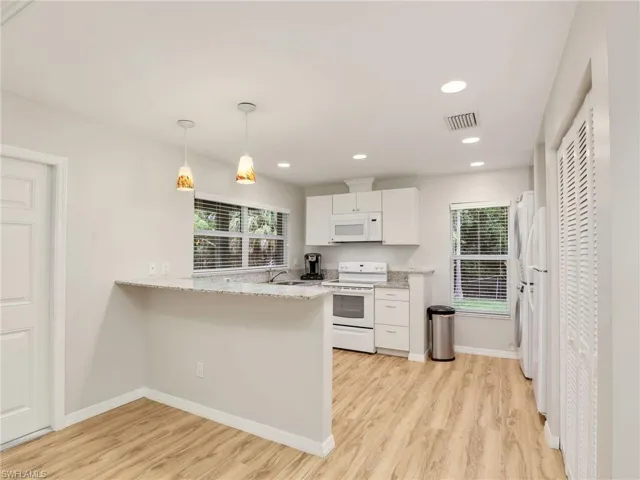 Kitchen featuring white appliances, light wood-style floors, white cabinetry, a peninsula, and recessed lighting