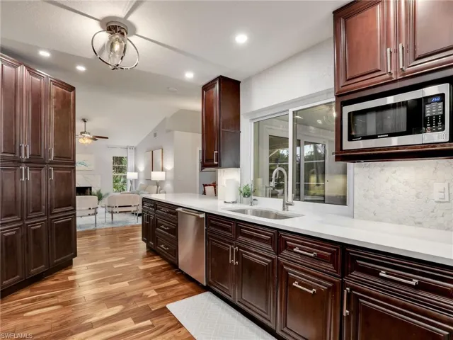 Kitchen with stainless steel appliances, decorative backsplash, light wood finished floors, lofted ceiling, and light countertops
