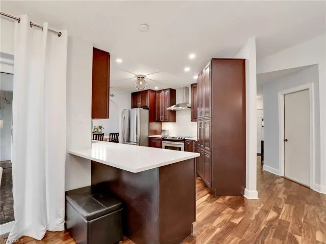 Kitchen with appliances with stainless steel finishes, wall chimney range hood, light wood-style flooring, recessed lighting, and a peninsula