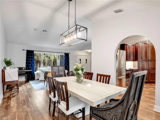Dining space with arched walkways, light wood-style floors, and lofted ceiling