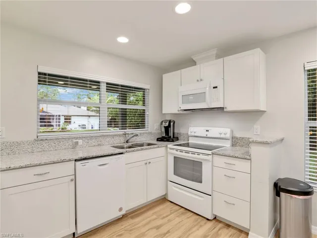 Kitchen with white appliances, white cabinets, light wood finished floors, recessed lighting, and light stone counters