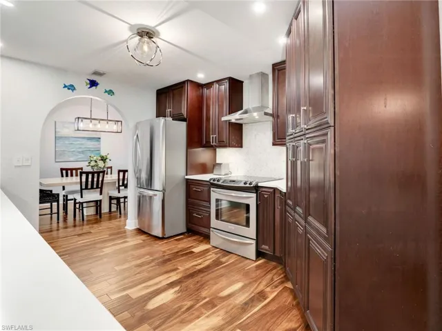 Kitchen featuring wall chimney range hood, appliances with stainless steel finishes, recessed lighting, light wood-style floors, and dark brown cabinetry