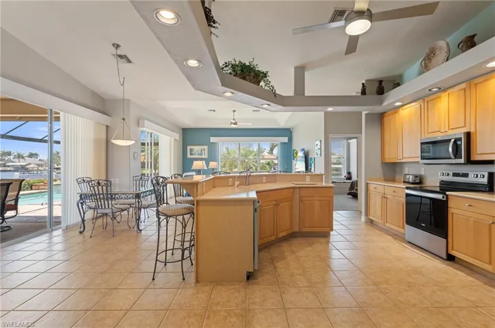 Kitchen with light tile patterned flooring, a kitchen bar, recessed lighting, a ceiling fan, and appliances with stainless steel finishes