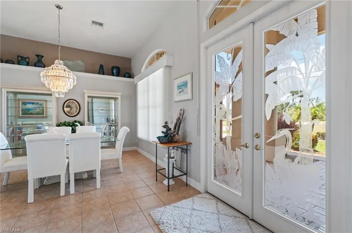 Dining room featuring light tile patterned flooring, a notable chandelier, french doors, a towering ceiling, and visible vents