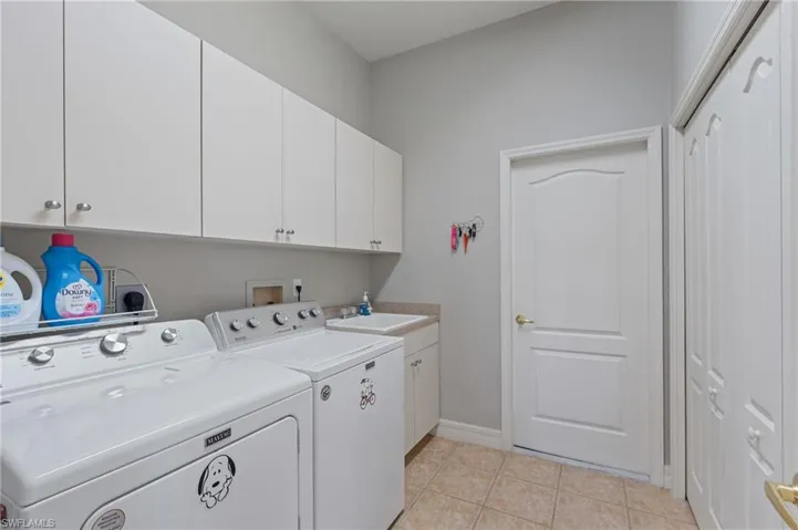 Laundry room with cabinet space, light tile patterned flooring, washing machine and clothes dryer, a sink, and baseboards