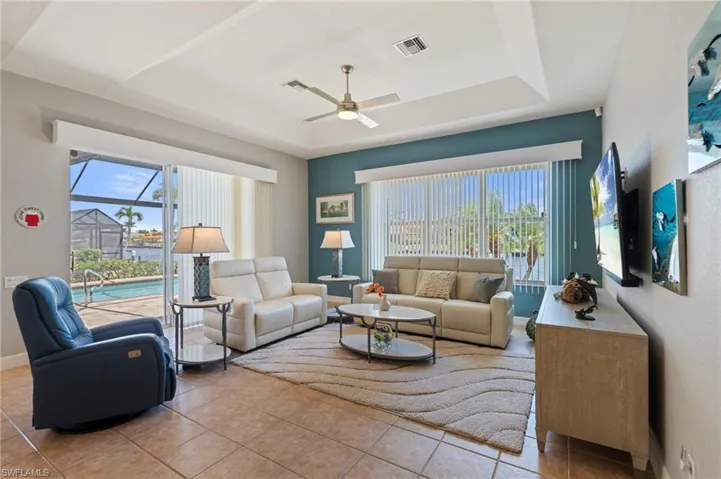 Tiled living area featuring visible vents, ceiling fan, a tray ceiling, and a wealth of natural light