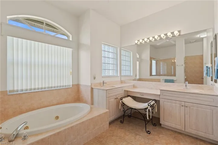 Bathroom with a ceiling fan, a tub with jets, a shower, vanity, and tile patterned floors