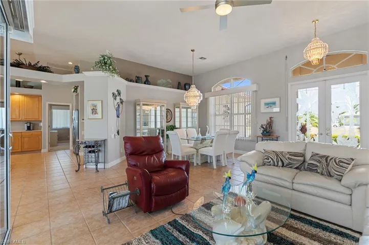 Living room with light tile patterned floors, baseboards, french doors, and ceiling fan with notable chandelier