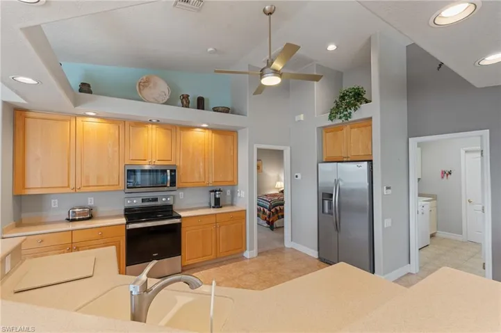 Kitchen featuring light tile patterned flooring, high vaulted ceiling, light countertops, a ceiling fan, and appliances with stainless steel finishes