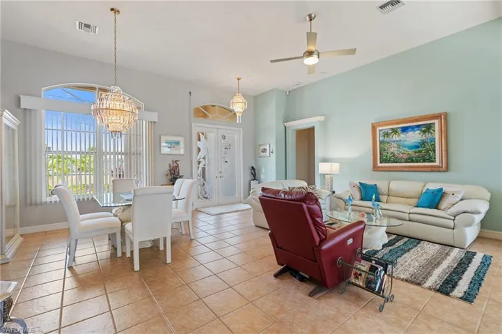 Living area with visible vents, baseboards, ceiling fan with notable chandelier, and light tile patterned flooring