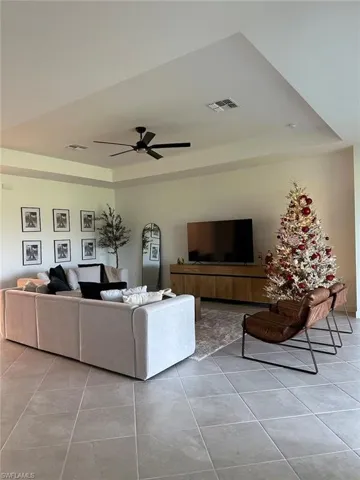 Living room featuring a raised ceiling, light tile patterned floors, and a ceiling fan