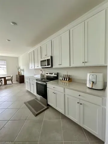 Kitchen with stainless steel appliances, white cabinetry, and light tile patterned floors