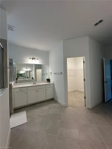 Full bath with vanity, a walk in closet, a shower with door, and light tile patterned flooring