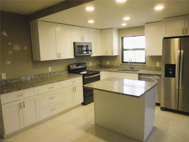 Kitchen featuring stainless steel appliances, white cabinetry, light stone counters, a center island, and recessed lighting