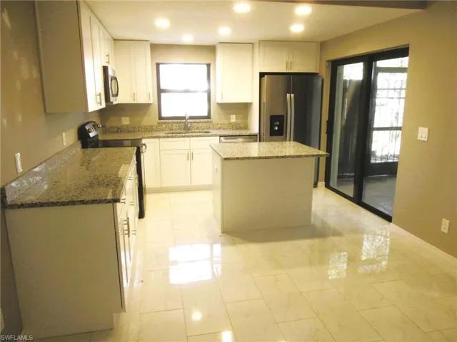 Kitchen with light stone countertops, stainless steel appliances, a kitchen island, white cabinets, and recessed lighting