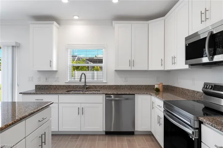 Kitchen featuring stainless steel appliances, light stone countertops, white cabinets, recessed lighting, and wood finish floors.