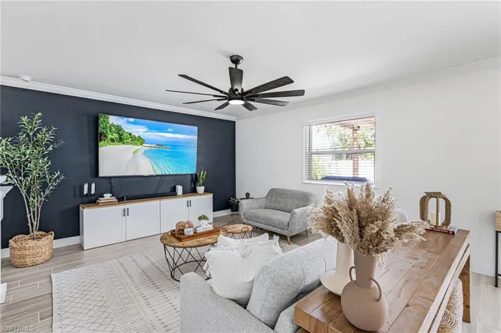Spacious living area featuring a dark accent wall, crown molding, and a contemporary ceiling fan