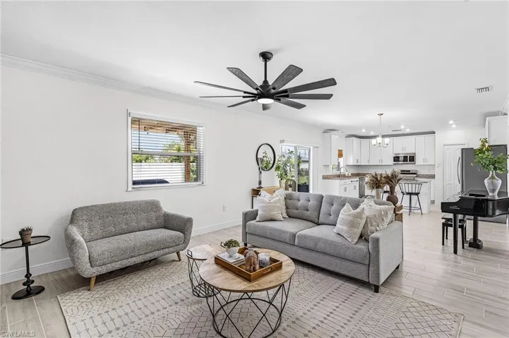 Open-concept living space featuring light-toned wood-finish flooring, a contemporary ceiling fan, and white crown molding