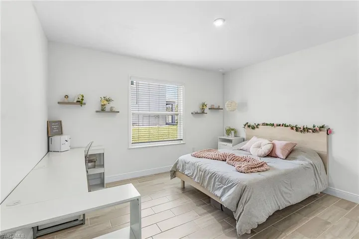 Bright interior bedroom 5 featuring wood-finish flooring, a large window with horizontal blinds, built-in recessed lighting, and a neutral color palette. First floor