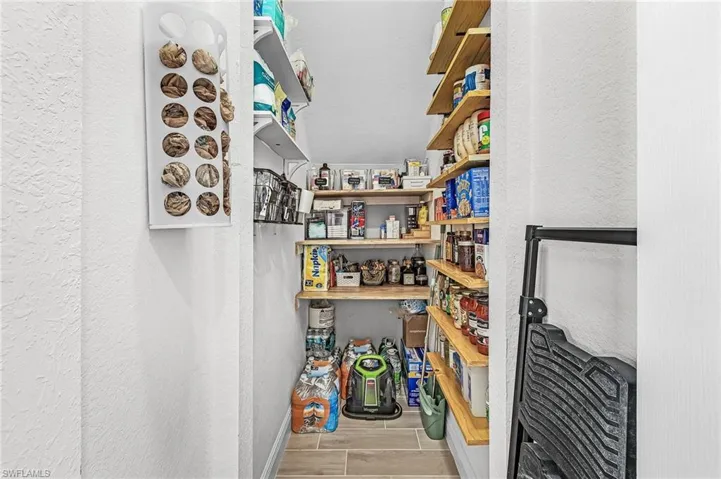 Walk-in pantry with light wood shelving, white walls, and wood-finish tile flooring