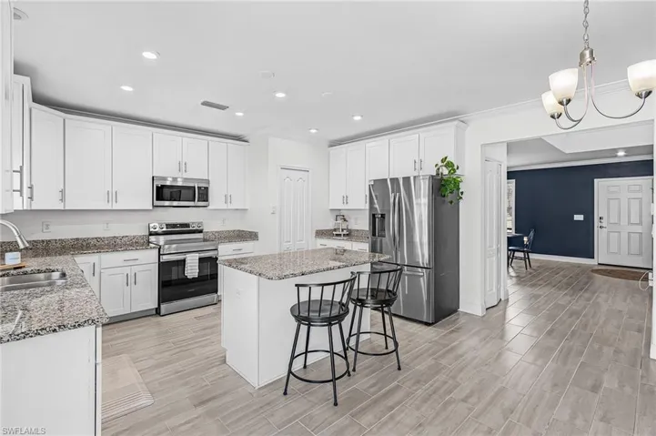 Kitchen featuring white cabinetry, granite countertops, stainless steel appliances, a center island with seating, and wood-look tile flooring