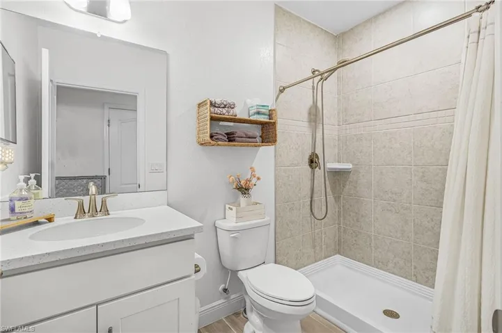 Bathroom 3 featuring a white vanity with an integrated sink, polished chrome faucet, a large wall mirror, and a shower with light-toned tile surround and a brushed nickel showerhead