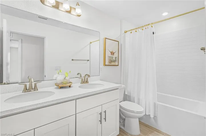 Bathroom 2 featuring a dual vanity with undermount sinks, a large wall-mounted mirror, and a combination tub/shower with subway tile surround