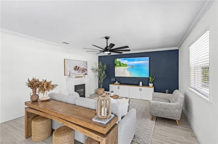 Living area featuring crown molding, tile flooring, a built-in fireplace with mantle, a dark accent wall, and a ceiling fan