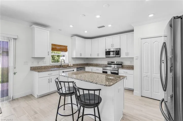 Contemporary kitchen featuring an island with a granite countertop, white shaker cabinetry, stainless steel appliances, and wood-finish tile flooring