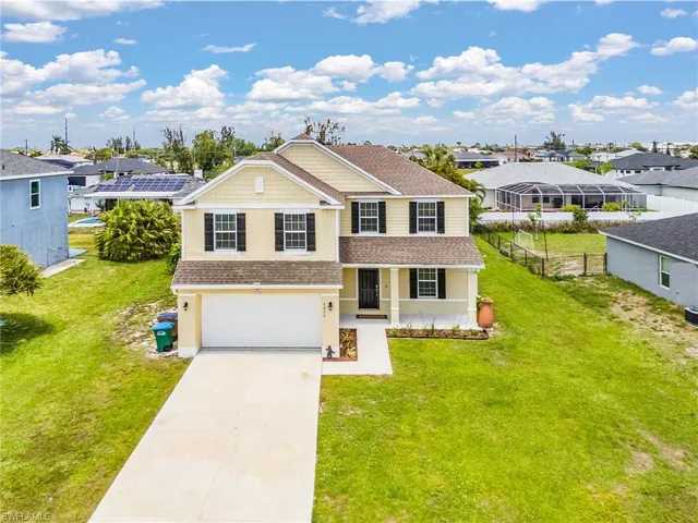 Two-story residence featuring a covered front porch, an attached garage, a paved driveway, and a spacious front lawn