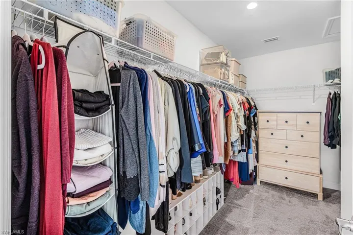 Expansive walk-in closet featuring wire shelving, multiple hanging rods, built-in shoe cubbies, and recessed lighting for primary bedroom