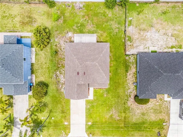 Aerial property view featuring a brown shingle roof, a concrete driveway, and a wooden deck