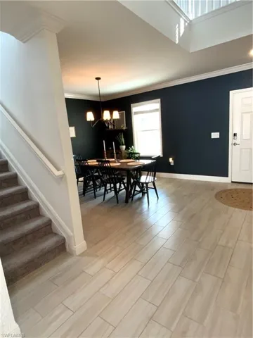 Dining room with stairway, wood tiled floors, a chandelier, crown molding, and a towering ceiling