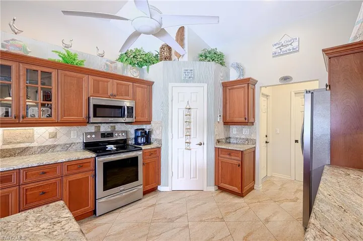 Kitchen with a ceiling fan, brown cabinetry, glass insert cabinets, backsplash, and appliances with stainless steel finishes