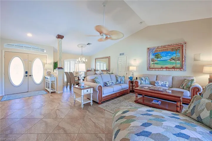 Living room with vaulted ceiling, visible vents, ceiling fan with notable chandelier, and french doors