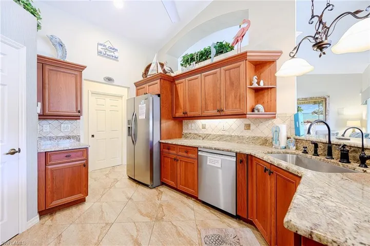 Kitchen with stainless steel appliances, a sink, backsplash, open shelves, and light stone countertops