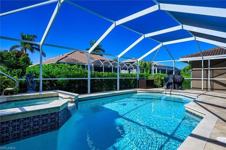 View of pool with a patio area, a pool with connected hot tub, glass enclosure, and a grill