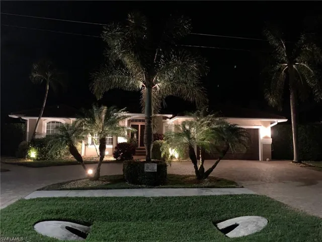 View of property hidden behind natural elements with stucco siding, a yard, a garage, and decorative driveway