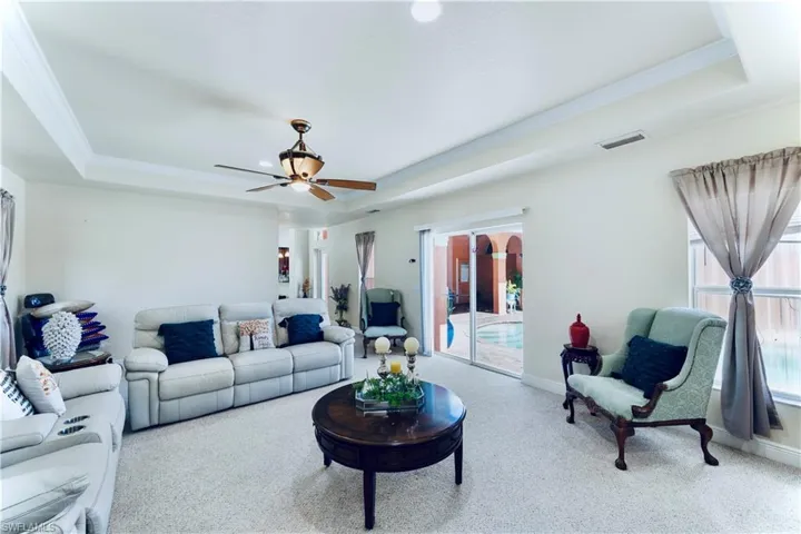 Living area with a tray ceiling, carpet floors, crown molding, and ceiling fan