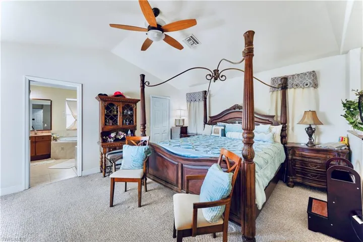 Carpeted bedroom featuring lofted ceiling, ensuite bath, and a ceiling fan