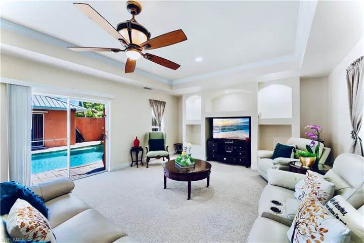 Living area with a raised ceiling, carpet flooring, a ceiling fan, ornamental molding, and built in features