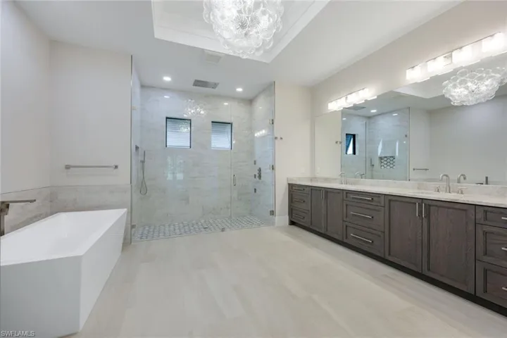 Bathroom with vanity, a notable chandelier, plus walk in shower, and a raised ceiling