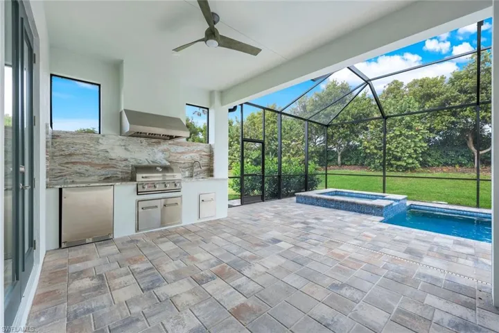 View of patio with sink, grilling area, glass enclosure, an in ground hot tub, and exterior kitchen