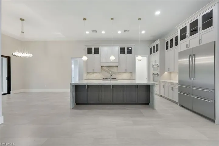 Kitchen with hanging light fixtures, appliances with stainless steel finishes, white cabinets, and a spacious island