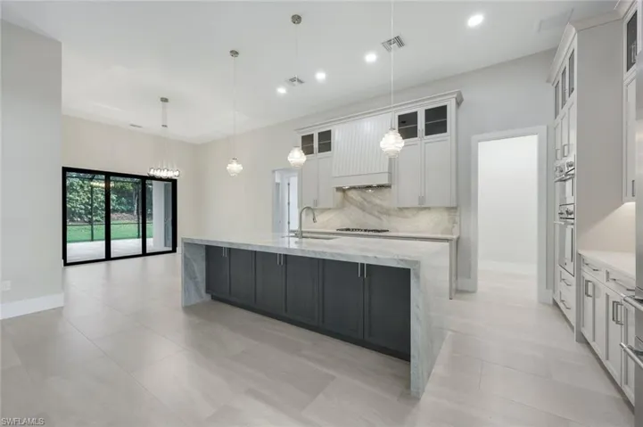 Kitchen with a spacious island, sink, white cabinetry, decorative light fixtures, and gas cooktop