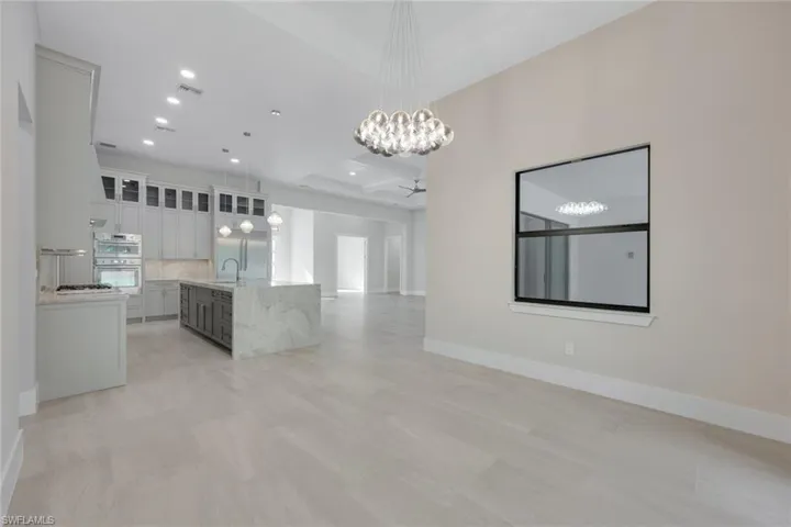 Kitchen featuring double oven, decorative light fixtures, white cabinetry, an island with sink, and light stone counters