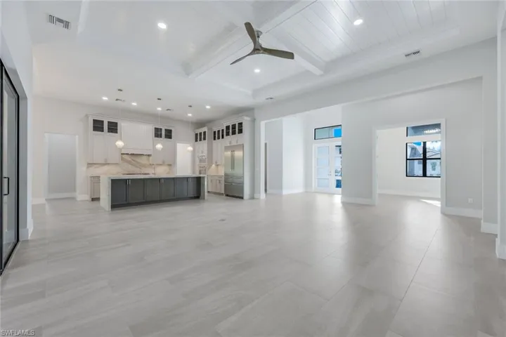 Unfurnished living room with beamed ceiling, ceiling fan, coffered ceiling, and a towering ceiling