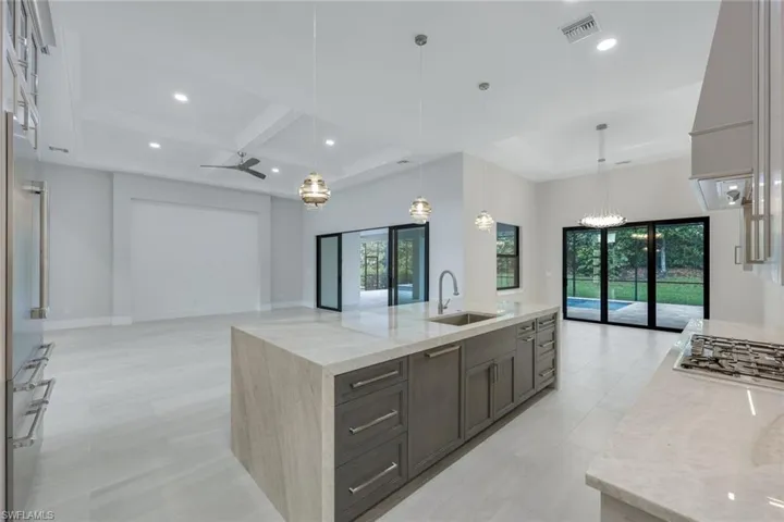 Kitchen with decorative light fixtures, sink, a large island with sink, light stone counters, and plenty of natural light