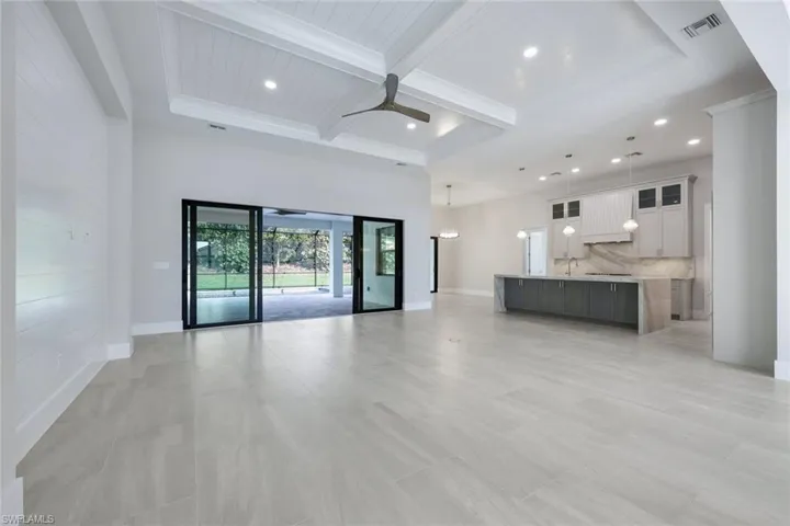 Unfurnished living room with sink, ceiling fan, beam ceiling, a high ceiling, and coffered ceiling