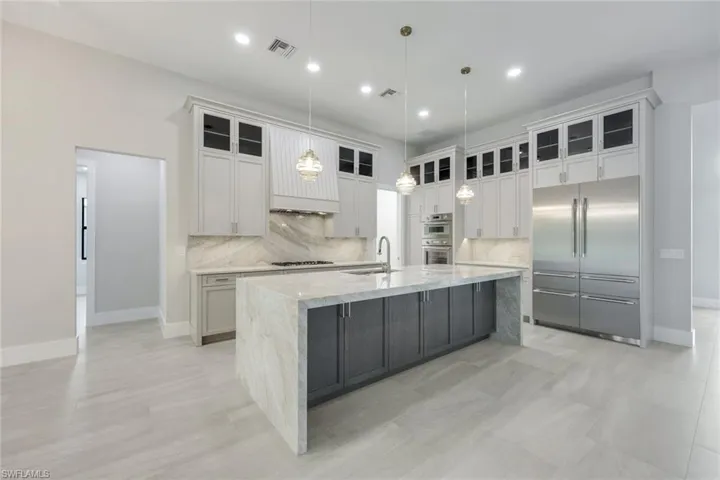 Kitchen featuring sink, appliances with stainless steel finishes, hanging light fixtures, white cabinets, and a large island with sink